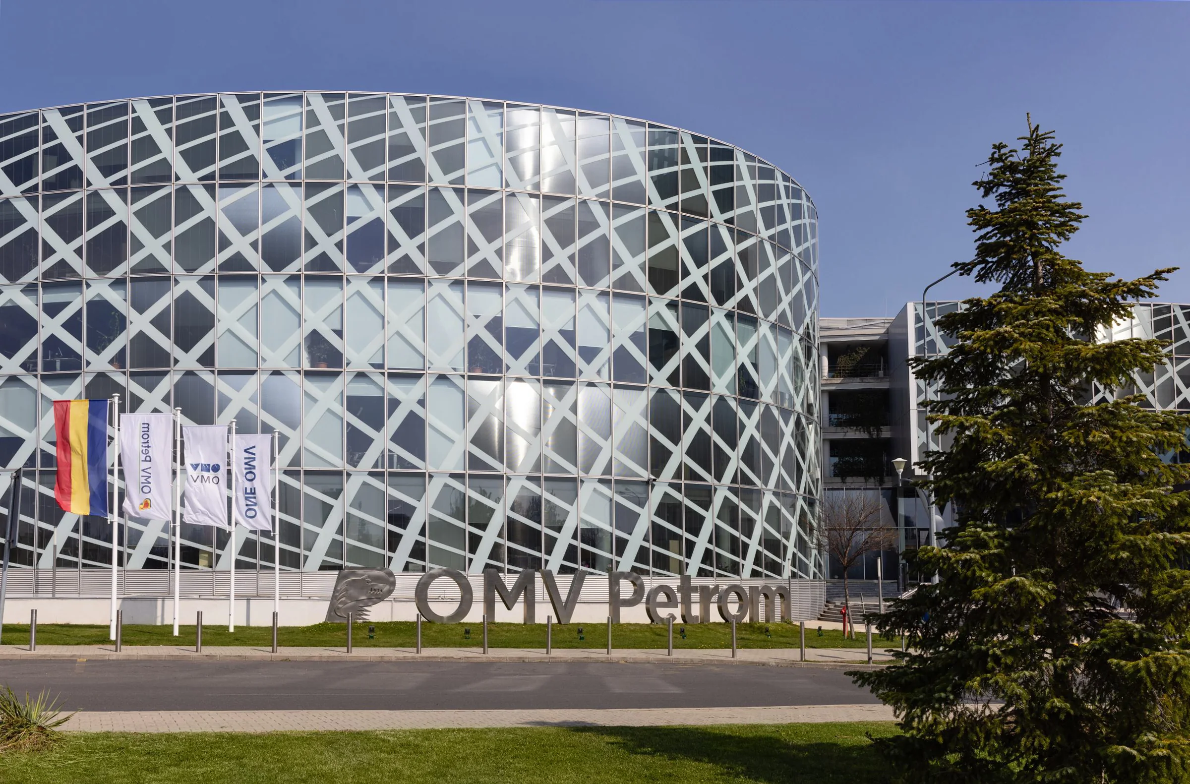 The OMV Petrom headquarters in Bucharest: a round glass building with a diagonal lattice facade, the company sign and flags in front